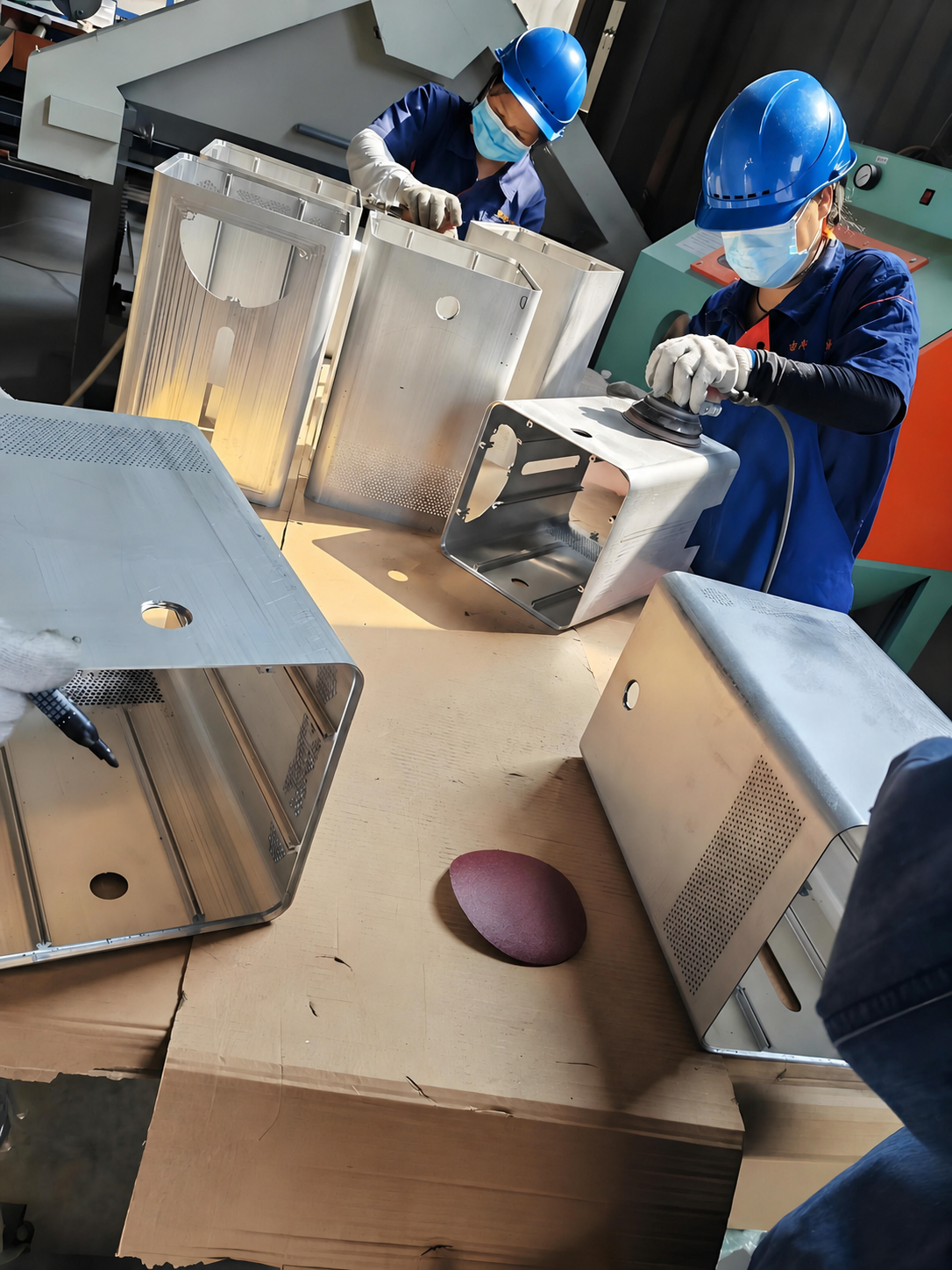 Operators preparing sheet-metal enclosures for finishing
